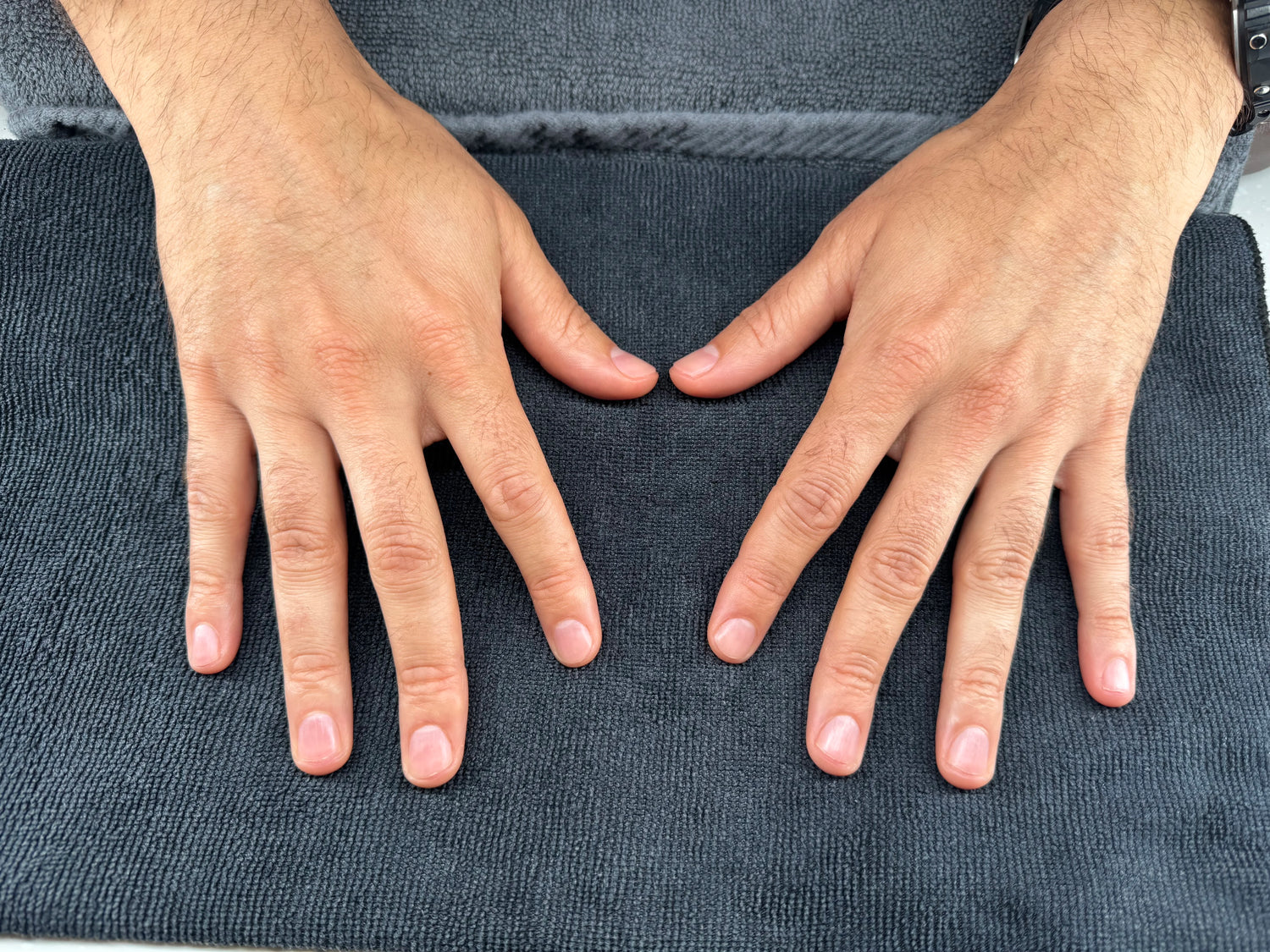Two hands making heart shapes on a textured gray surface after a men's manicure
